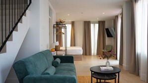 Un salon moderne avec un canapé, une petite table sur laquelle repose un livre, un lit et un téléviseur à l’arrière-plan.