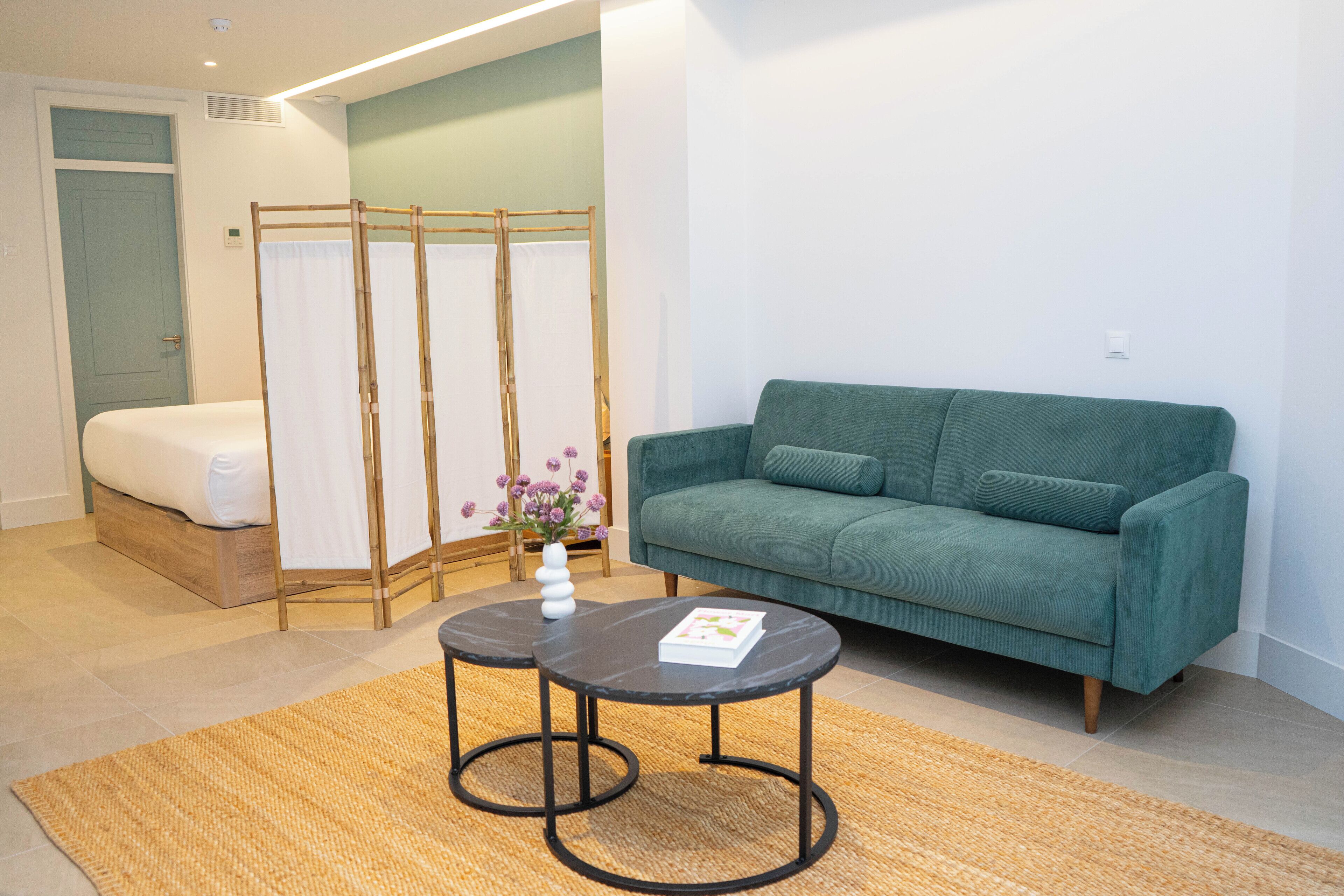 A modern room with a bed, a green sofa, two round tables, and a bamboo screen.