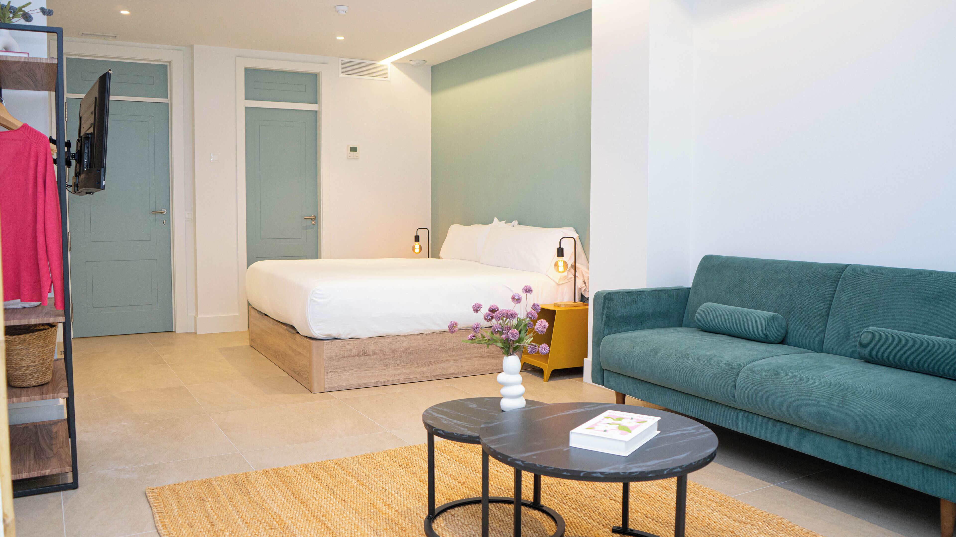 Une chambre à coucher avec un lit, un canapé vert, une petite table et une table de chevet.