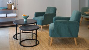 Un salon moderne avec des fauteuils turquoise, une petite table ronde et un tapis tissé.