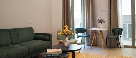 Una sala de estar moderna con un sofá verde, una mesa de centro con libros, un jarrón con flores y un comedor con sillas y una mesa.