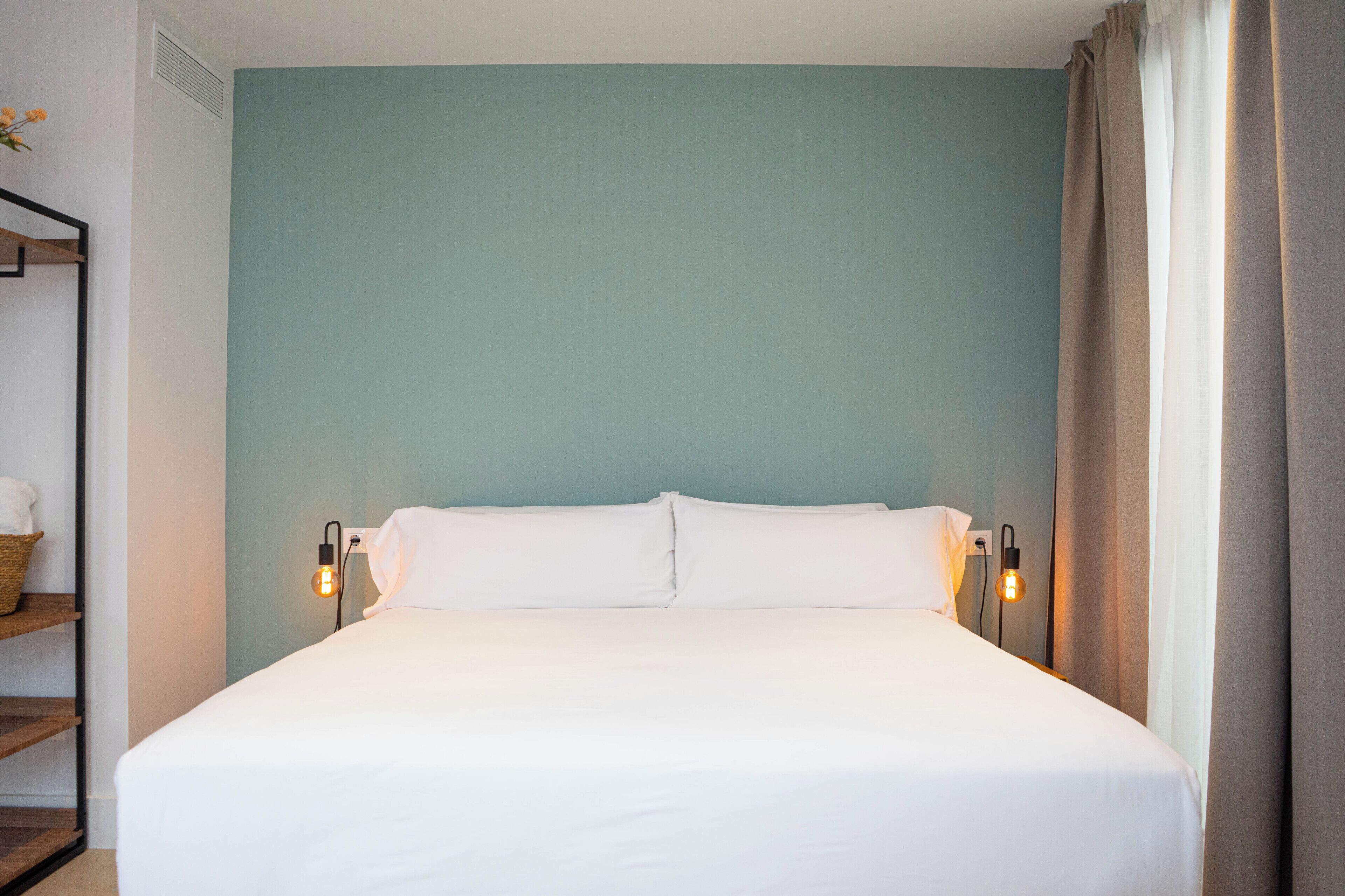 Una cama bien hecha con sábanas blancas, dos lámparas de noche y una pared color turquesa.