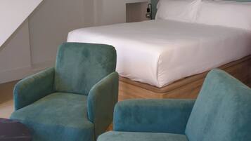 A bedroom with a bed, two teal armchairs, a small table, and a staircase.