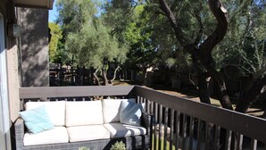 A covered outdoor seating area with a wicker sofa, two potted plants, and a wooden deck railing.