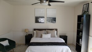 A bedroom with a bed, a ceiling fan, a nightstand, a chair, and a bookshelf.