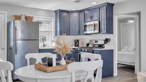 A modern kitchen with blue cabinets, a stainless steel refrigerator, and a dining area with white chairs and a round table. - Fast WiFi | Linen+Towels | Espresso | Pet Friendly (Seaside Heights)