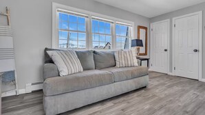 A modern living room with a grey sofa, large windows, and a ceiling fan. - Fast WiFi | Linen+Towels | Espresso | Pet Friendly (Seaside Heights)