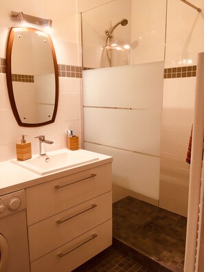 Een moderne badkamer met een wastafel, spiegel, douche en toilet.
