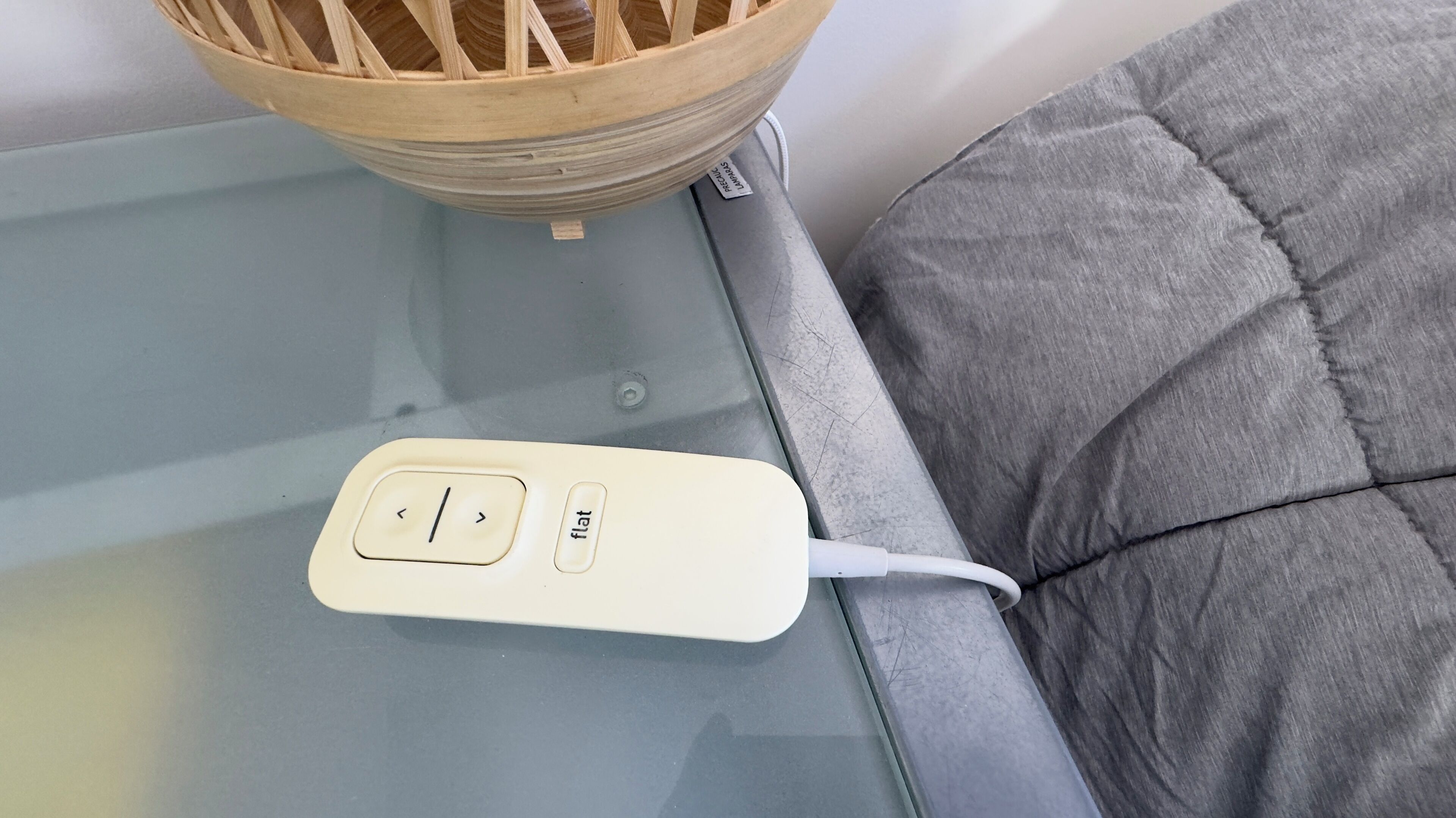 A power strip on a glass table with a grey cushion and a wooden basket.