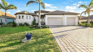 A two-story house with a garage, a well-maintained lawn, and palm trees. - Surfside Villa ~ Entire home in Cape Coral, Florida (Cape Coral)