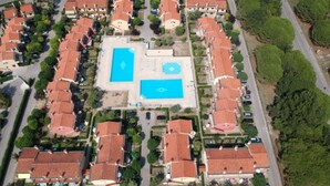 Vue aérienne d’un quartier résidentiel composé de maisons aux toits rouges uniformes, avec une piscine centrale et un espace vert bien entretenu.