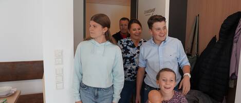 Eine vierköpfige Familie in einem modernen Wohnzimmer mit einer Holzbank, einem Esstisch mit Schüssel und einer Wand mit einem Schild.