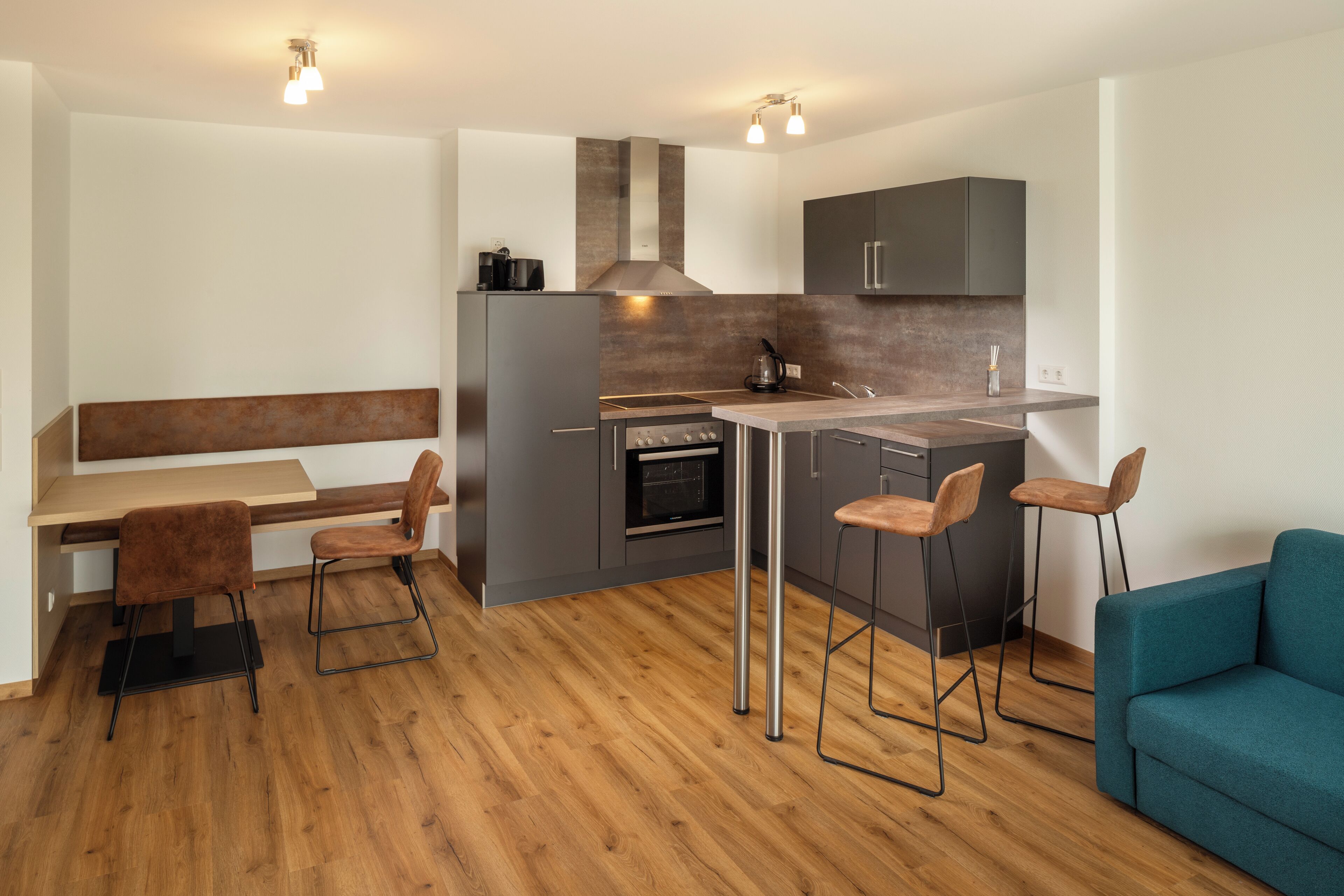 A modern kitchen with a central island, bar stools, and a teal sofa.