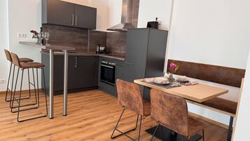A modern kitchen with dark cabinets, a central island, and a dining area with a wooden table and cushioned chairs.