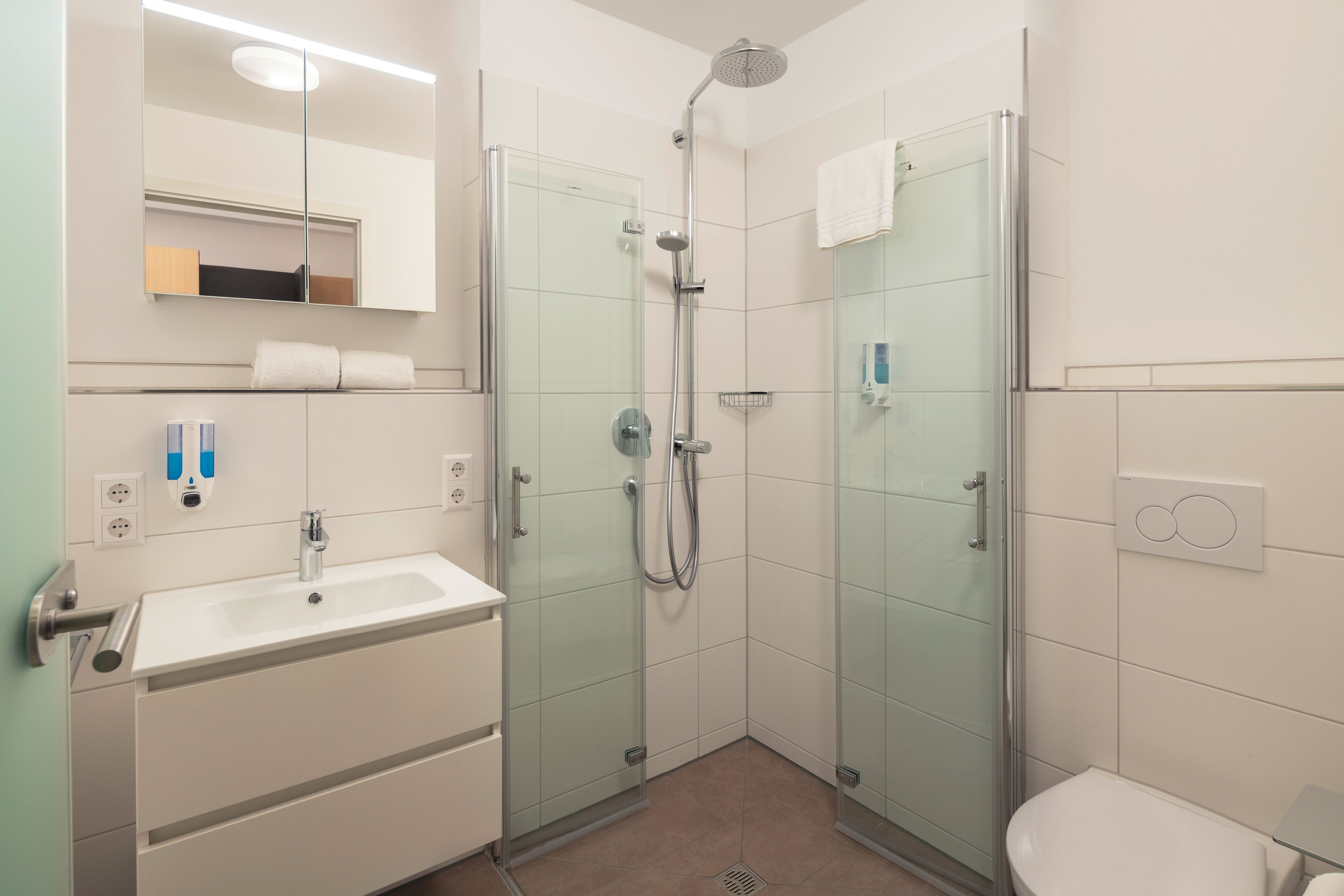 Een moderne badkamer met een glazen douchecabine, een witte wastafel en een toilet.