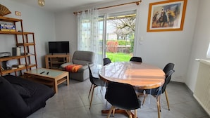 A living room with a sofa, coffee table, TV, bookshelf, and a dining table with chairs. - Quiet, flower-filled house in the countryside, good location, easy access (Le Grand-Lemps)