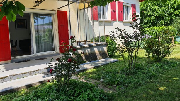 A house with a red door, a sliding glass door, and a small garden with plants and a bench. - Quiet, flower-filled house in the countryside, good location, easy access (Le Grand-Lemps)