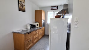 A compact kitchen with wooden cabinets, a white refrigerator, and a microwave on the counter. - Quiet, flower-filled house in the countryside, good location, easy access (Le Grand-Lemps)