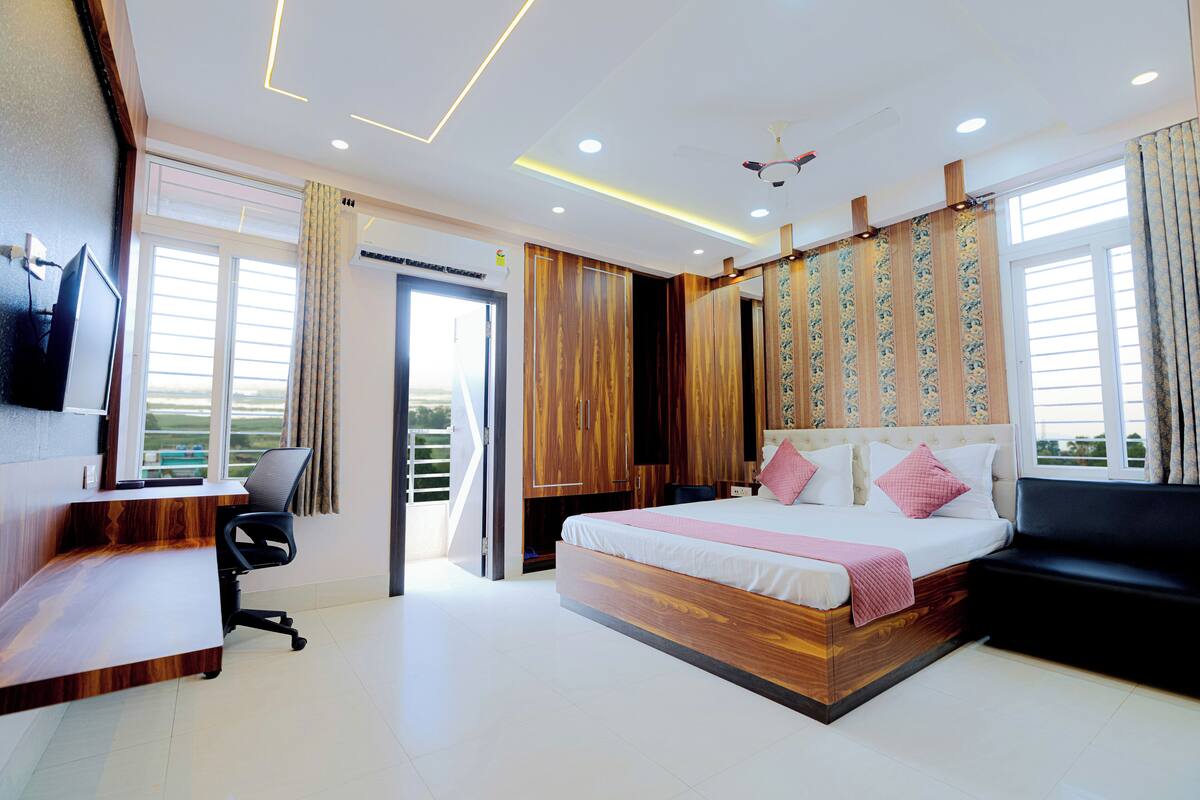 A modern bedroom with a wooden desk, a bed with a headboard, a black sofa, and a TV mounted on the wall.