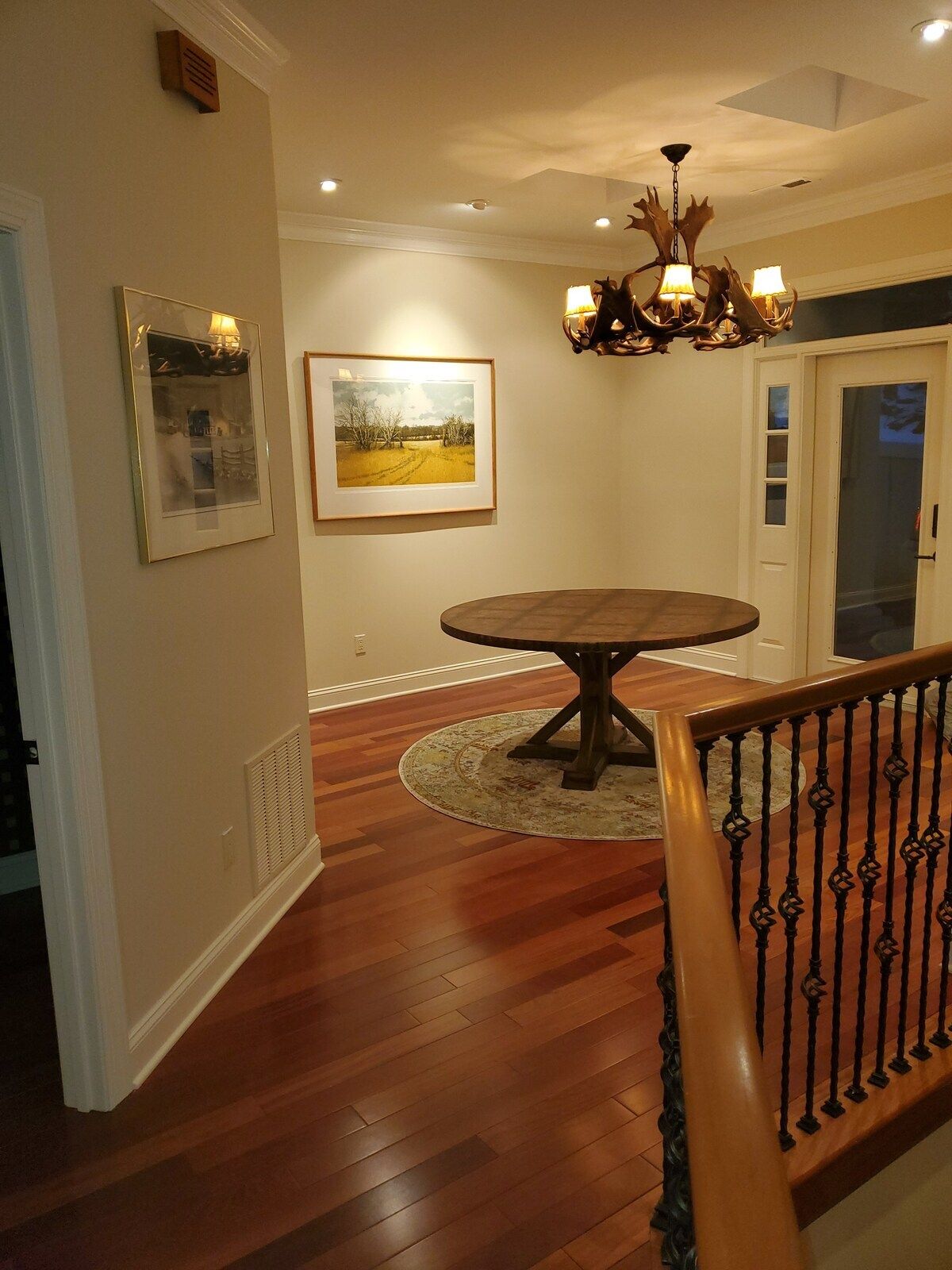 A dining area with a round table, a chandelier, and framed pictures on the wall.