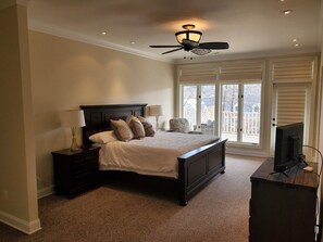 Une chambre à coucher comprenant un lit, des tables de chevet, un ventilateur de plafond et un téléviseur.