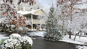A residential property with a covered driveway, snow-covered trees, and a two-story house with a balcony.
