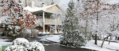 A residential property with a covered driveway, snow-covered trees, and a two-story house with a balcony.
