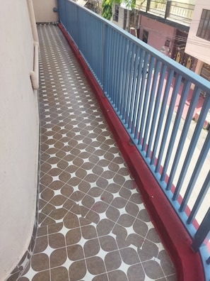 Ein Balkon mit gemustertem Boden, einem blauen Geländer und Blick auf umliegende Gebäude.