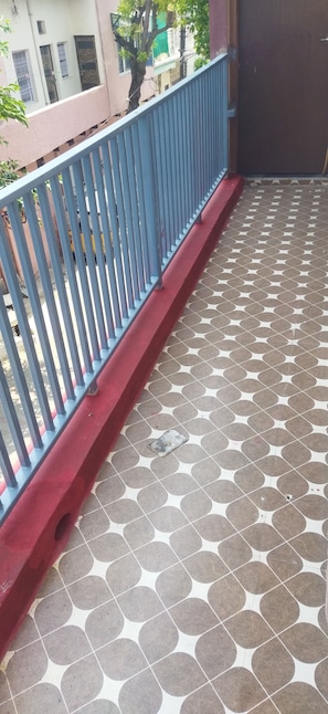 Ein Balkon mit einem gemusterten Boden, einem blauen Geländer und einem roten Sockel.