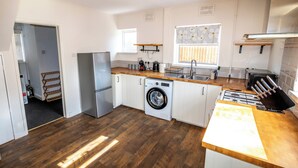 A modern kitchen with white cabinets, a stainless steel refrigerator, a washing machine, and a gas stove. - 3 Bed Home - Sleeps 8 - Stoke City fc - Parking (Stoke-on-Trent)