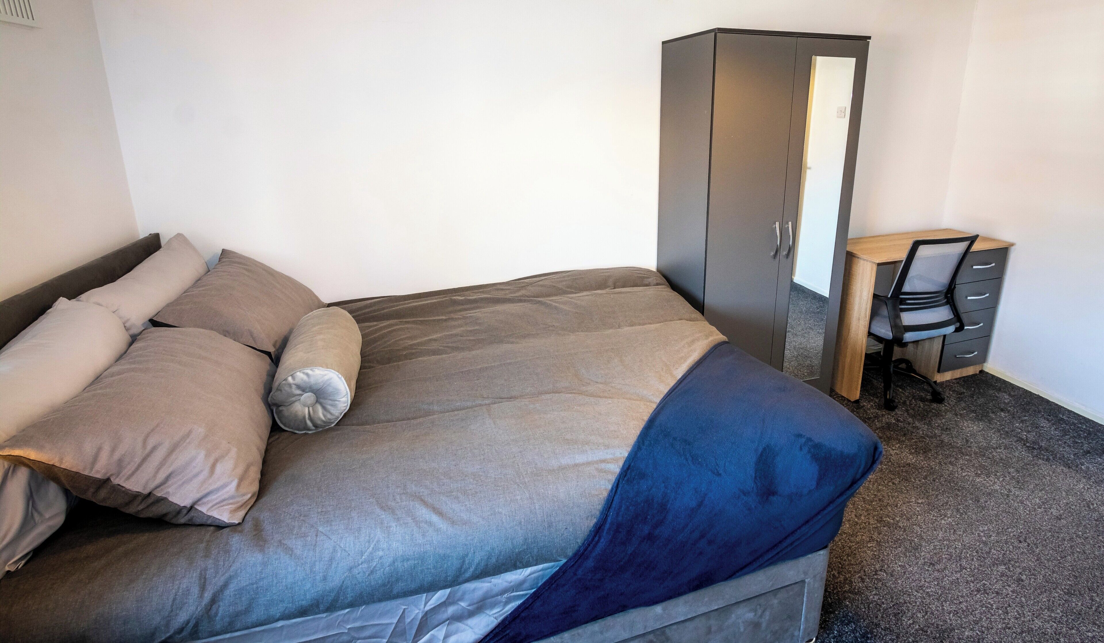 A bedroom with a bed, a desk, and a wardrobe.