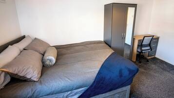 A bedroom with a bed, a desk, and a wardrobe.