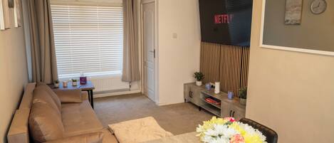 A living room with a sofa, a coffee table with a vase of flowers, a TV, and a dining area with chairs.