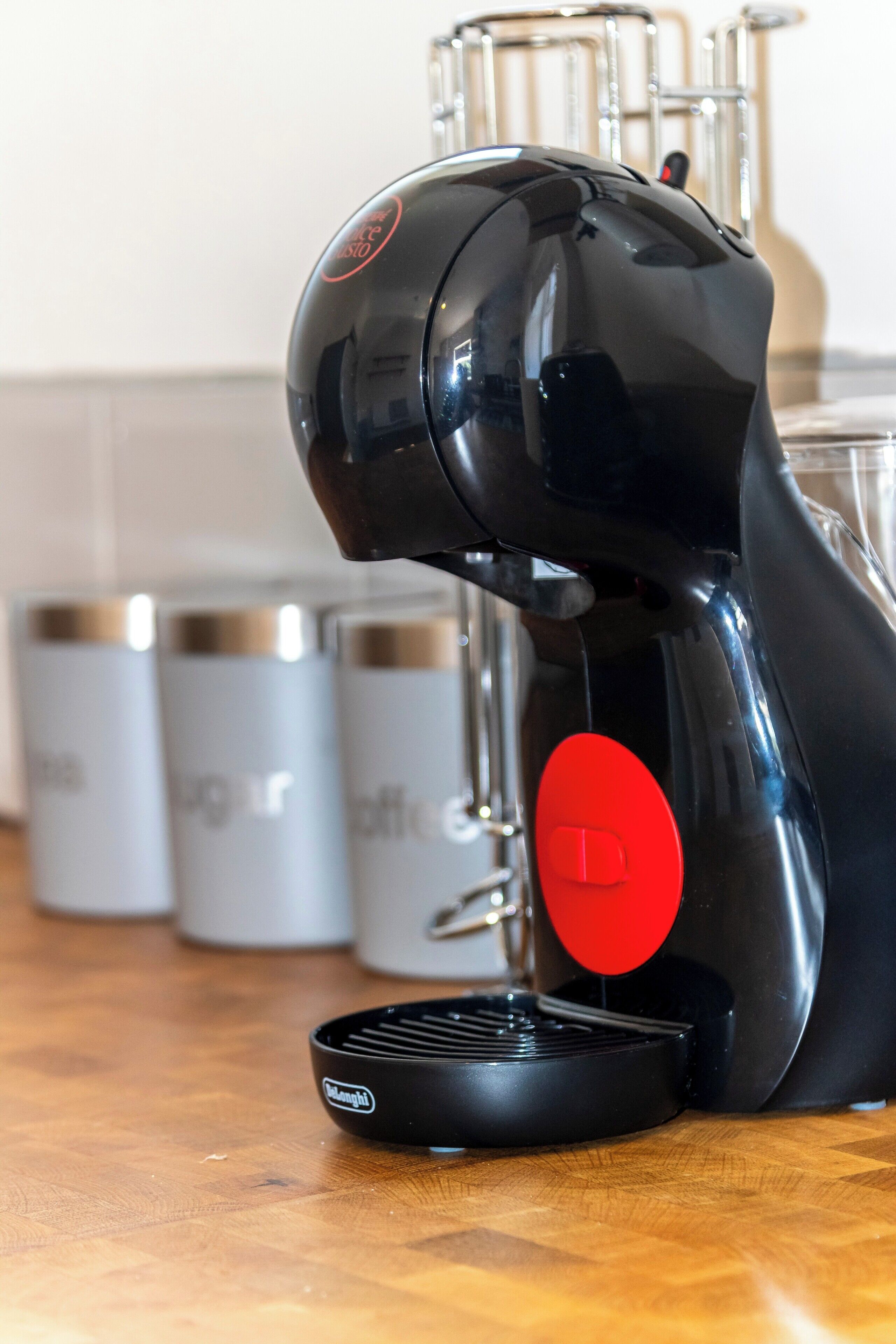 Máquina de café expresso preta com um botão vermelho sobre uma bancada de madeira.