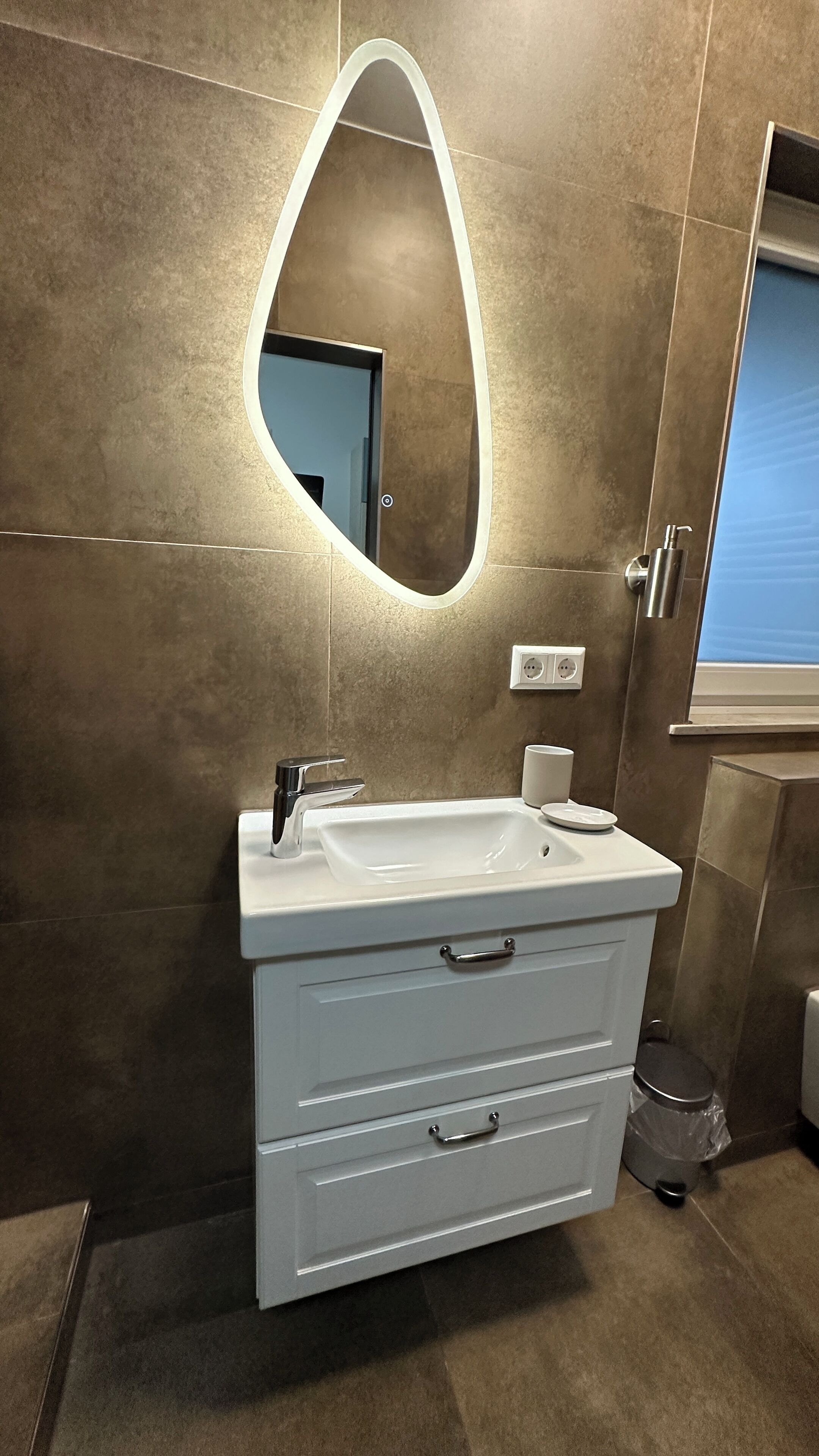 Une salle de bain moderne avec un meuble-lavabo blanc, un miroir avec éclairage intégré et des toilettes.