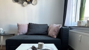 A modern living room with a dark grey sofa, a white coffee table, and a decorative wall piece. - HARMONY "4" 1-room apartment with kitchen (Gütersloh)