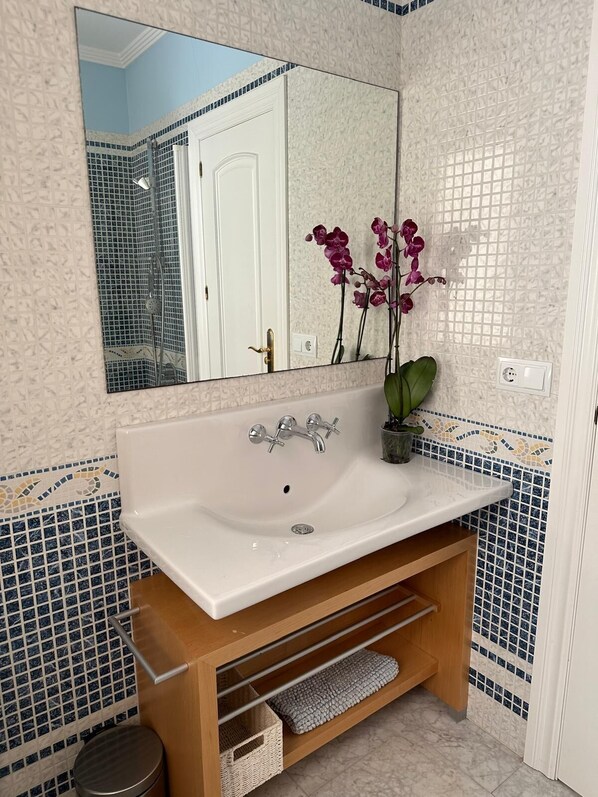 A bathroom with a white sink, a mirror, a potted orchid, and a tiled wall with a geometric pattern.