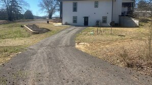 A single-story house with a dark roof, a front porch, and a driveway leading to the entrance.