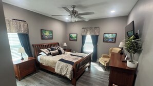 A bedroom with a bed, a desk, a chair, a ceiling fan, and a wall-mounted TV.