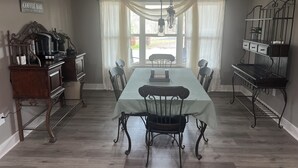 A dining room with a long table, chairs, a coffee station, and a kitchen area.