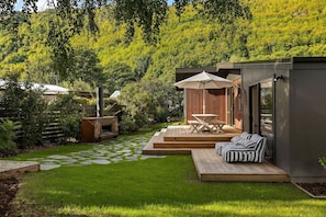 Un patio moderno al aire libre con un sendero de piedra, una terraza de madera y una zona de estar con cojines a rayas.