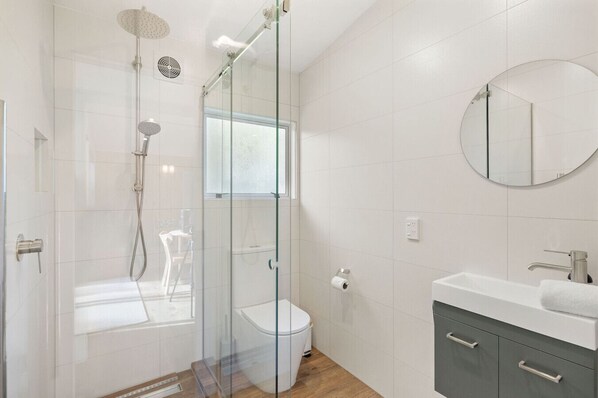 Un baño moderno con ducha envuelta en vidrio, inodoro, lavabo con espejo y suelo de madera.