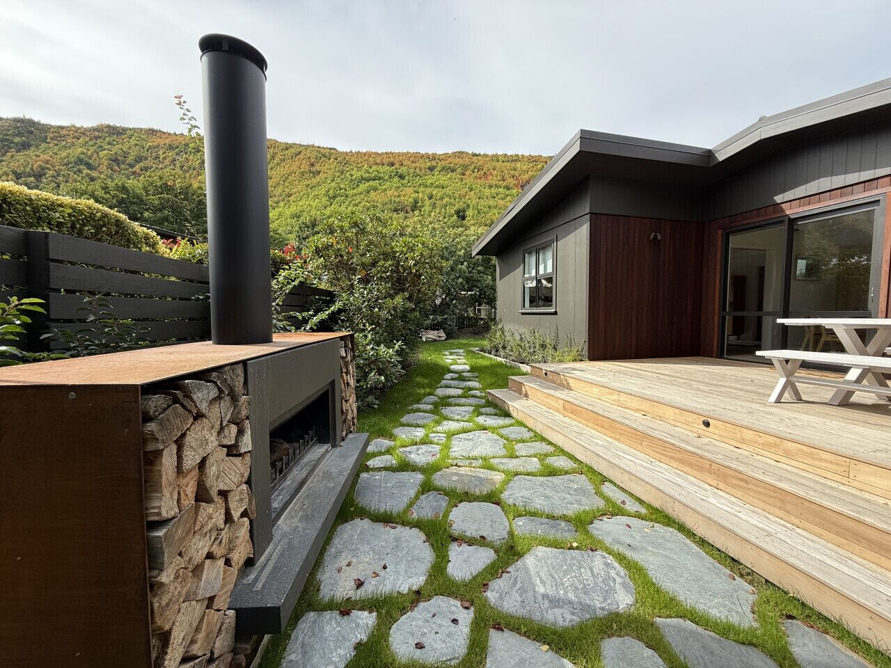 A stone pathway leading to a wooden deck with a modern house in the background.
