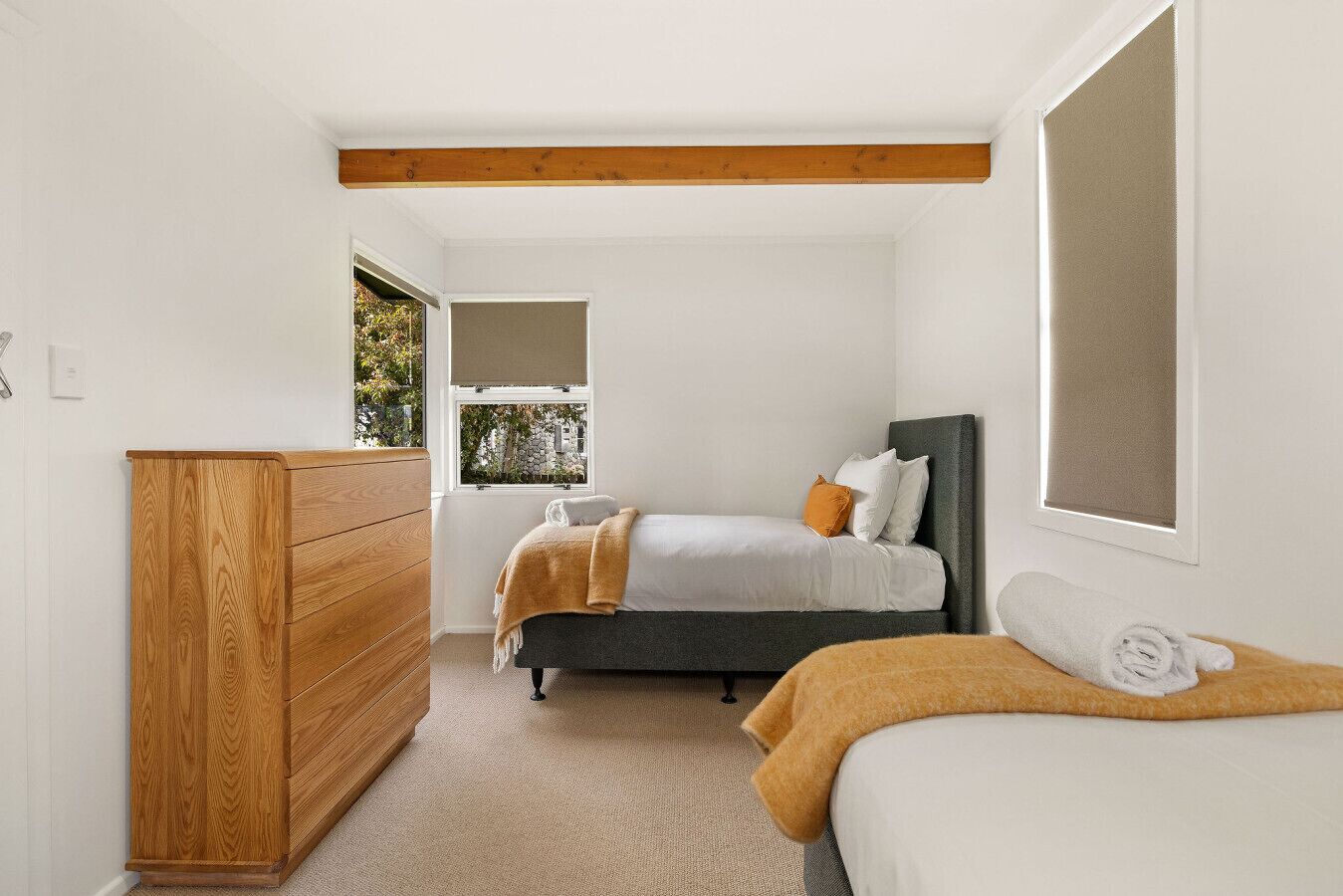 Een slaapkamer met een houten dressoir, een bed met een grijze hoofdbord en een raam met uitzicht op groen.