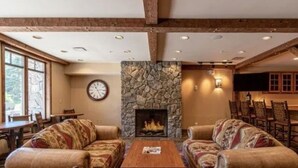 Ein gemütliches Wohnzimmer mit Kamin aus Stein, zwei gemusterten Sofas, einem Holztisch und einem Essbereich mit Stühlen.