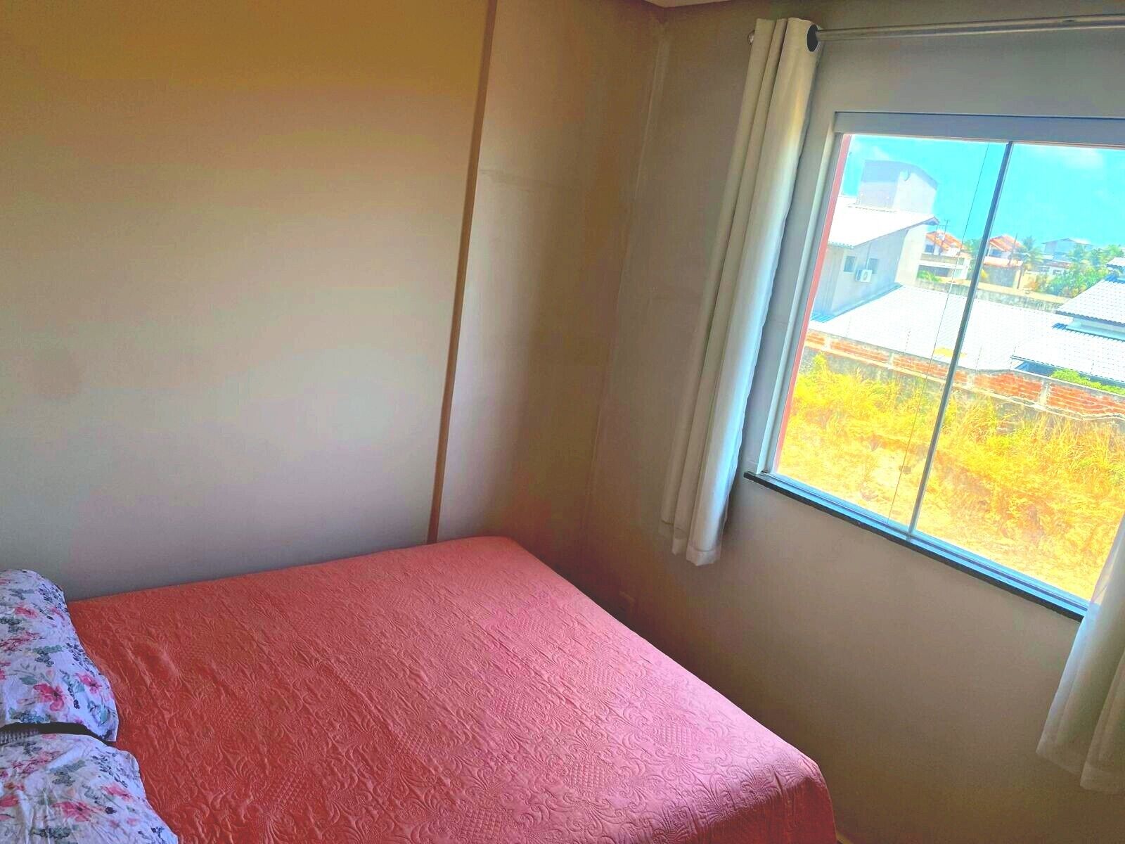 Een kleine kamer met een enkel bed, een raam met gordijnen en uitzicht op gebouwen.