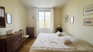 Ein Schlafzimmer mit Bett, Kommode, Stuhl und einem Fenster mit Vorhängen.