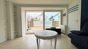 Ein Zimmer mit einem weißen Tisch, einem blauen Sofa und einer Glasschiebetür, die auf eine Terrasse mit einer Steinmauer und einem weißen Zaun führt.