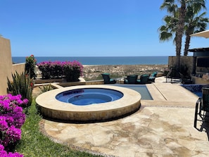 A circular hot tub with a stone border, surrounded by a patio area with outdoor furniture and a view of the sea. - Novaispania Estates Governor (Cabo San Lucas)
