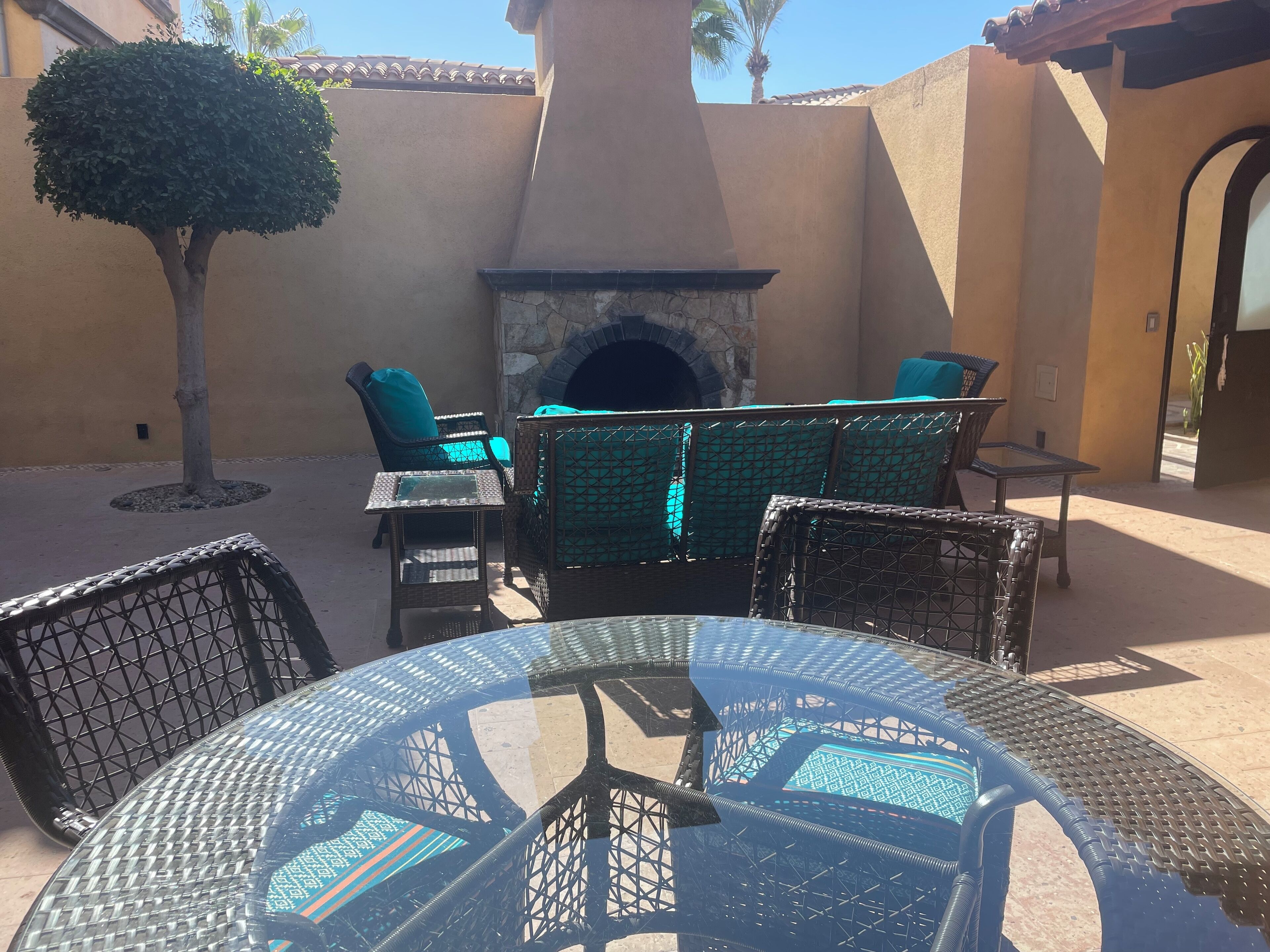An outdoor patio with wicker furniture, a glass table, and a stone fireplace.
